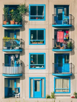 “Beige apartment building with blue window frames and balconies filled with green plants.